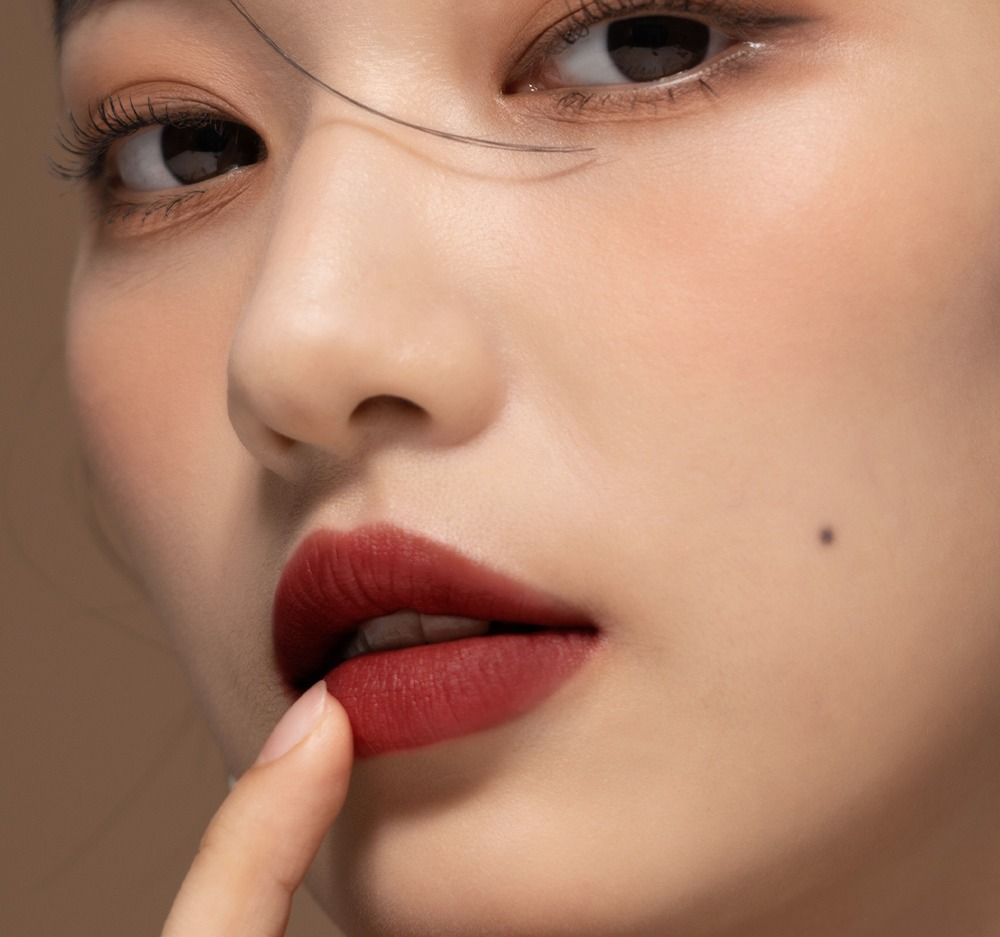 Gros plan d'un visage avec des lèvres rouge foncé. Un doigt touche les lèvres. Teint clair.