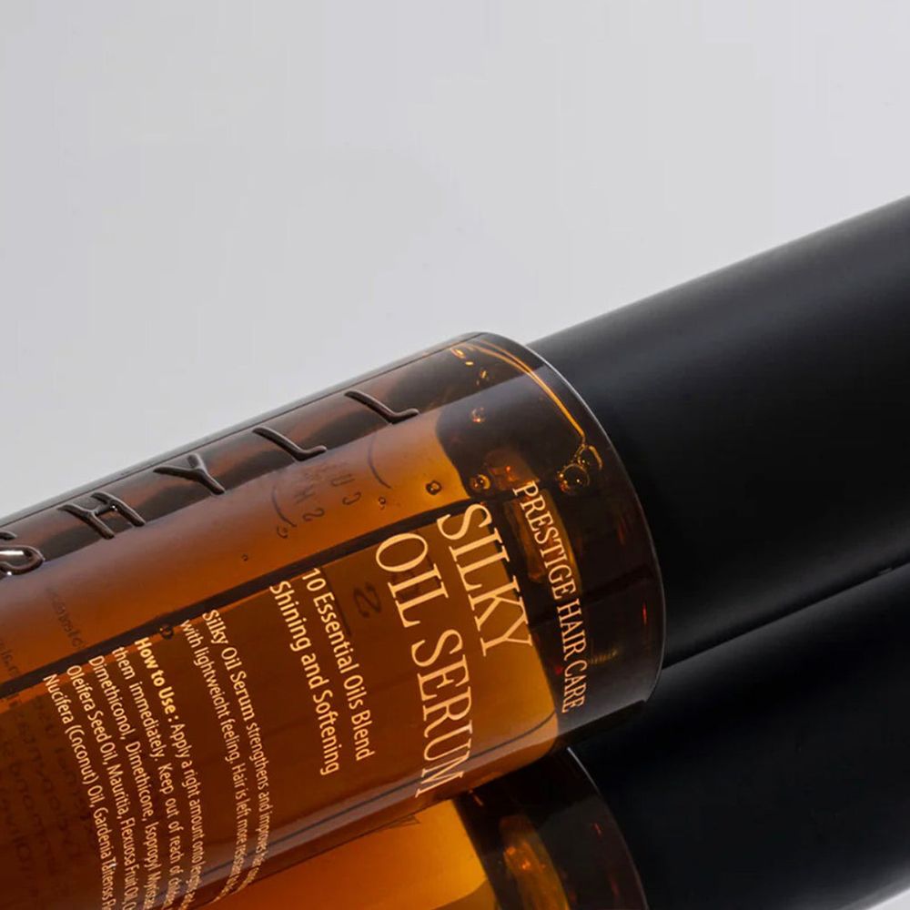 Close-up van een bruine haaroliefles met zwarte dop. Opschrift: Silky Oil Serum. Voor professionele haarverzorging.