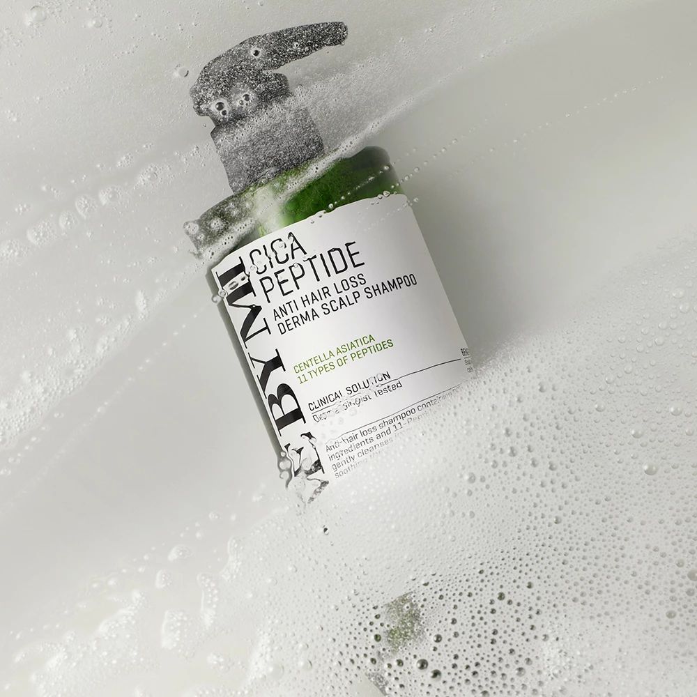 Flacon de shampooing vert avec pompe dans des bulles de savon. Inscription : Cica Peptide Anti Hair Loss Derma Scalp Shampoo.