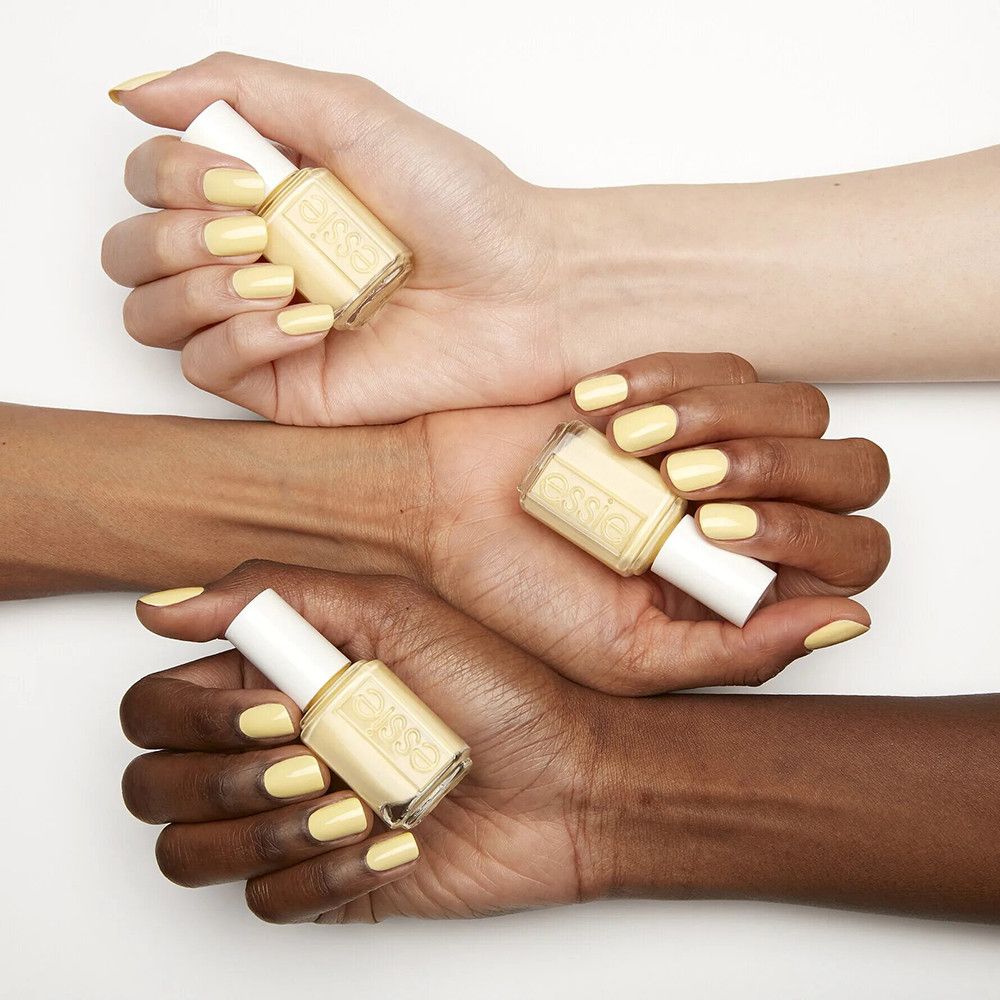 Trois mains tenant des flacons de vernis à ongles. Ongles vernis en jaune. Flacons avec bouchon blanc, étiquette.