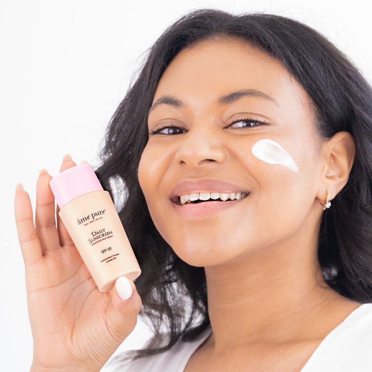 Une femme applique de la crème solaire SPF 50 sur son visage, tenant le flacon.