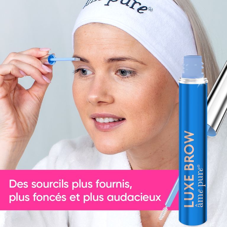 Une femme portant un bandeau applique le sérum pour sourcils LUXE BROW. Le flacon bleu avec applicateur argenté est bien visible.