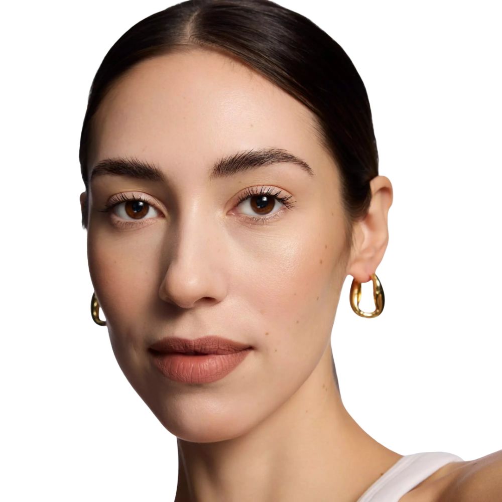 Portrait d'une femme portant du rouge à lèvres. Boucles d'oreilles dorées. Teint et couleur des lèvres visibles. Lumière naturelle.