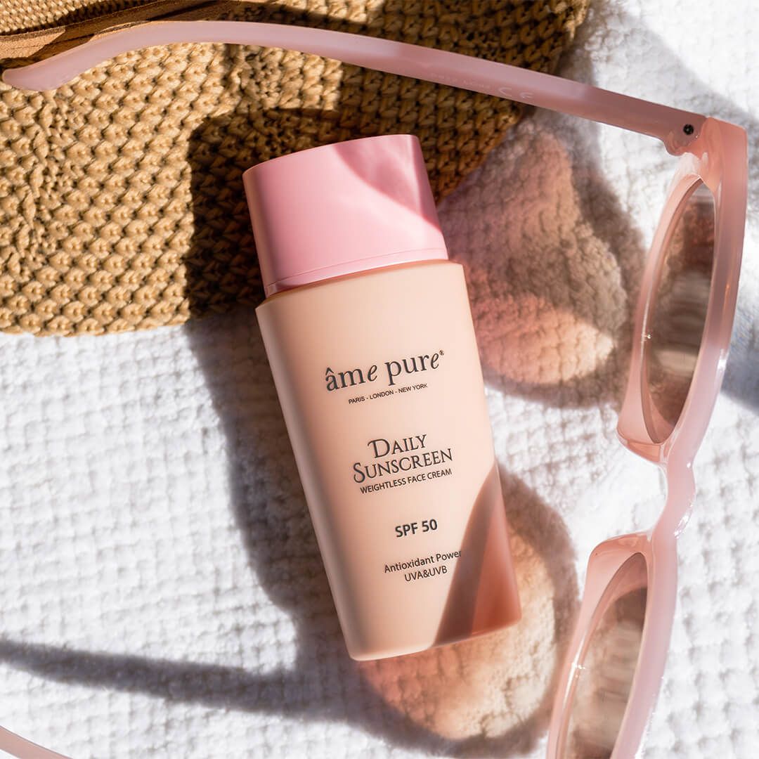 Âme Pure Daily Sunscreen fles naast zonnebril en tas, SPF 50.