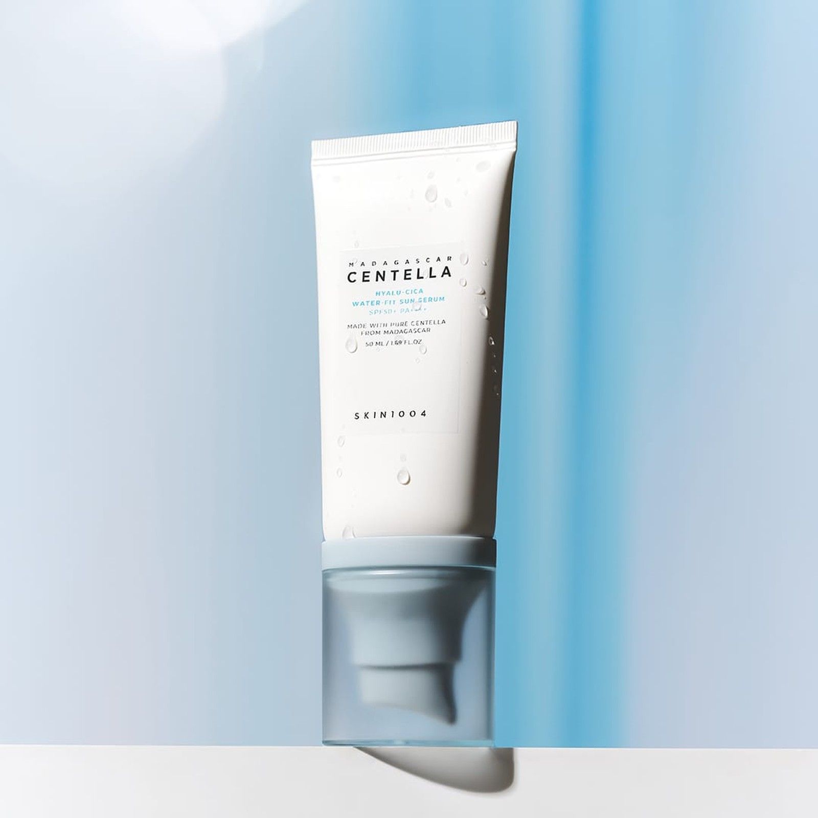 SKIN1004 Hyalu-Cica Water-Fit Sérum Solaire SPF 50+ PA++++ avec des gouttes d'eau sur le tube, sur fond bleu.