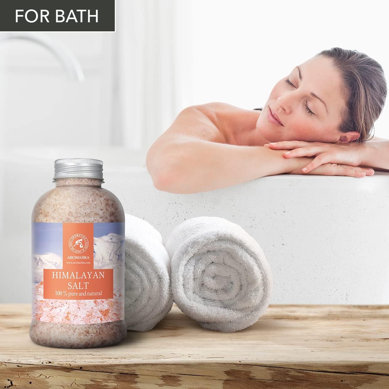Bouteille de sel d'Himalaya pour le bain, avec deux serviettes roulées à côté.