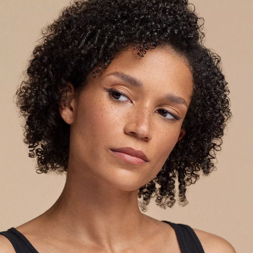 Portrait d'une femme aux cheveux bouclés. Elle regarde de côté. Maquillage des yeux appliqué.