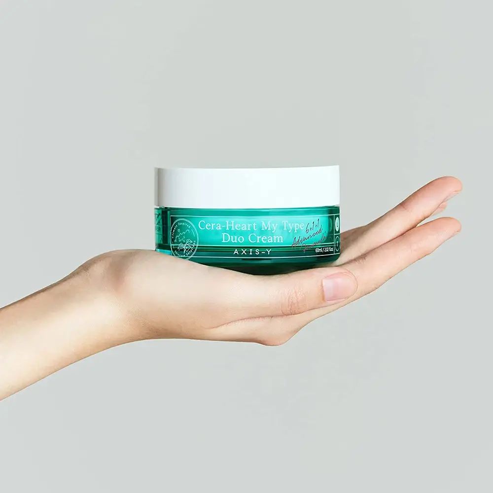 Hand houdt groene crème pot met witte deksel. Opschrift: Cera-Heart My Type Duo Cream. Merk: AXIS-Y.