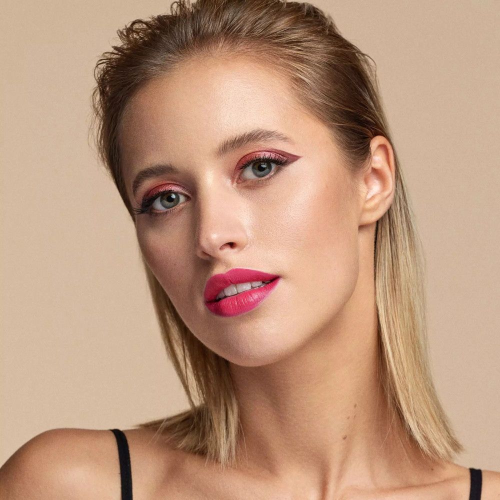 Portret van een vrouw met roze lippenstift en oogschaduw. Ze draagt een zwarte tanktop. Haar haar is blond.