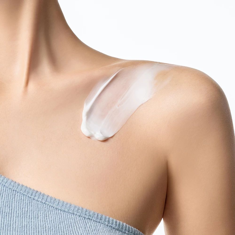 Lichte huid met crème aangebracht op de schouder. Blauwe top.