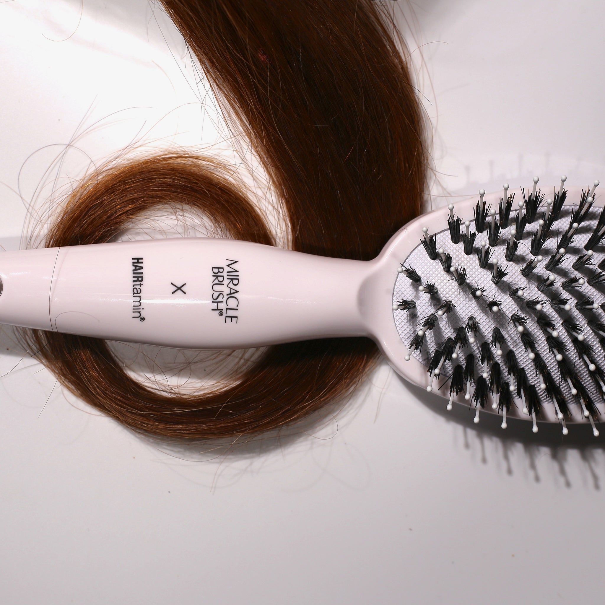 Witte borstel met zwarte borstelharen en een haarstreng. Opschrift MIRACLE BRUSH X HAIRtamin.