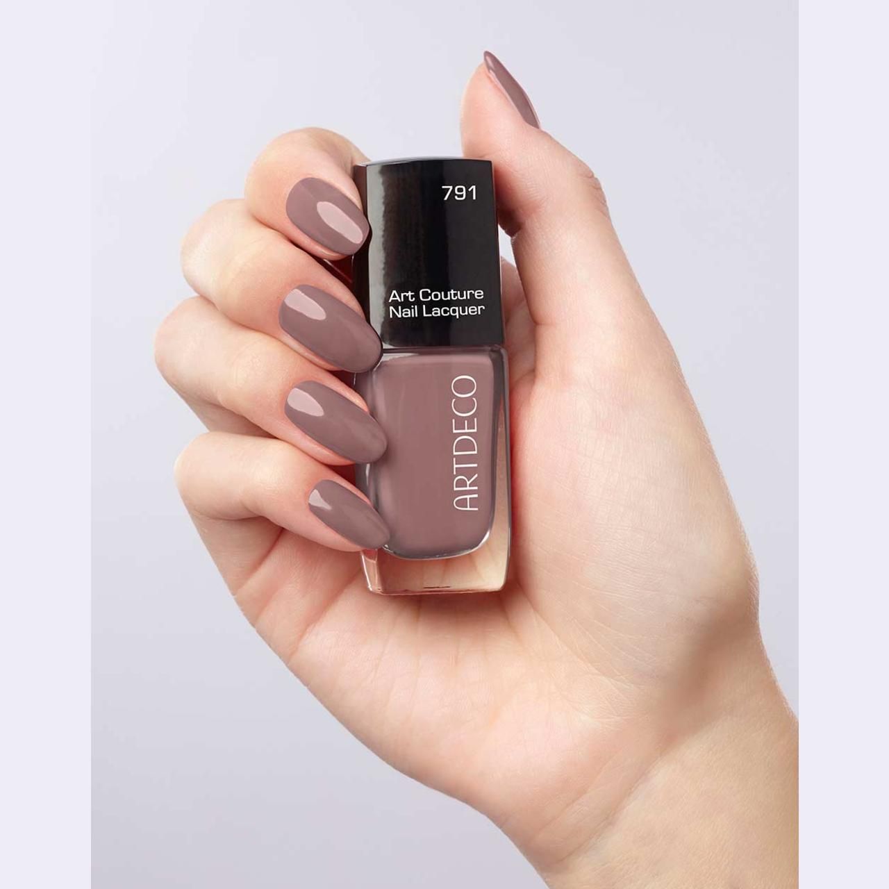 Hand houdt Artdeco Art Couture nagellak en gelakte nagels vast. Nagellakfles met zwarte dop. Nagels gelakt in bijpassende kleur.