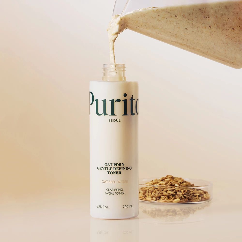 Toner wordt in een fles gegoten. Daarnaast haverkorrels. Opschrift: Purito, Oat PDRN Gentle Refining Toner.
