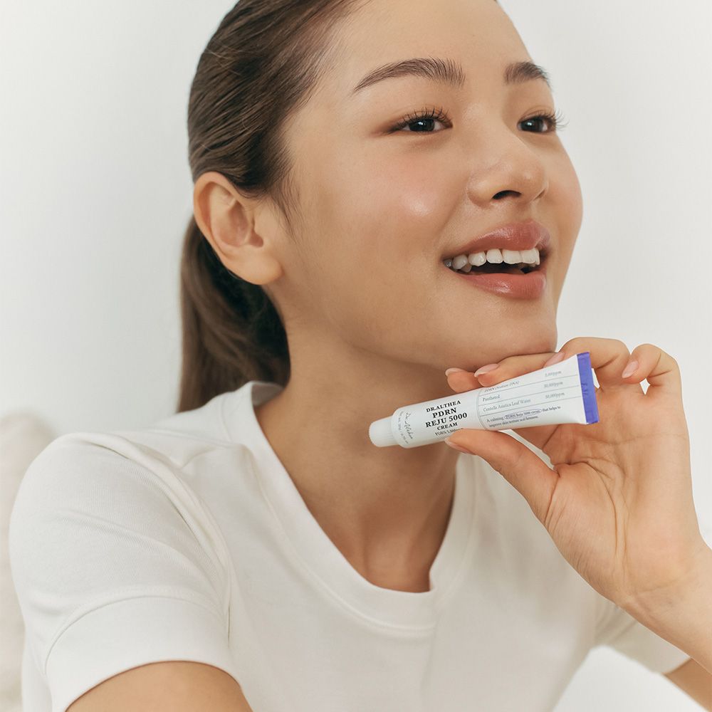 Een vrouw houdt een Dr.Althea PDRN Reju 5000 Cream tube bij haar nek.