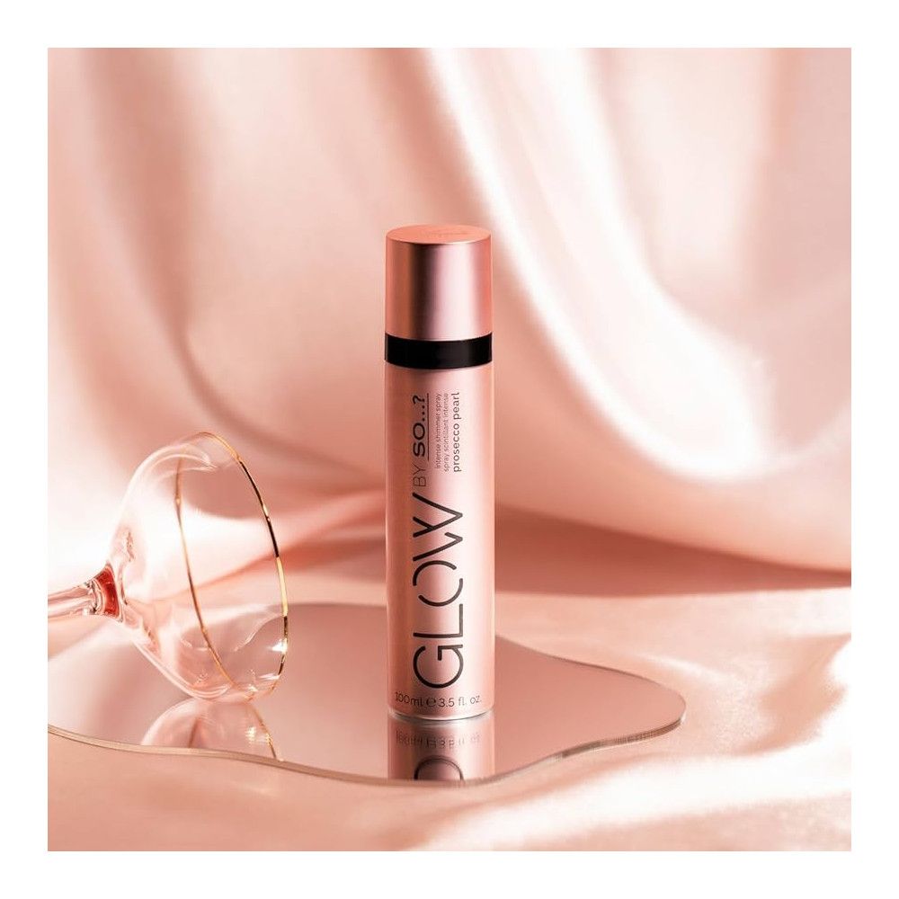 Flacon de brume rose sur miroir. Inscription : GLOW BY SO...? Prosecco Pearl. En arrière-plan : tissu et verre.
