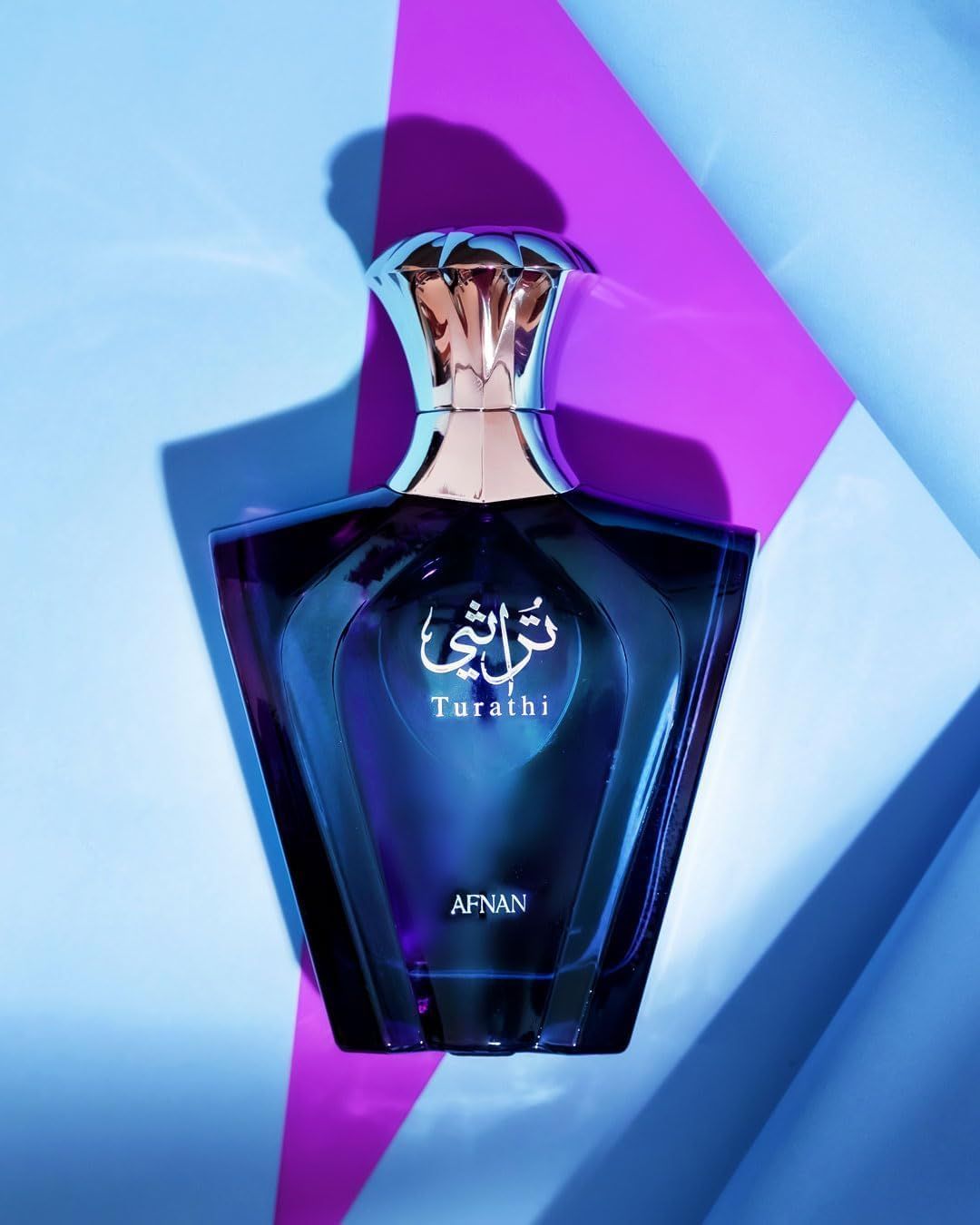 Flacon de parfum bleu avec bouchon argenté. Inscription "Turathi" et "AFNAN". Fond avec formes géométriques.