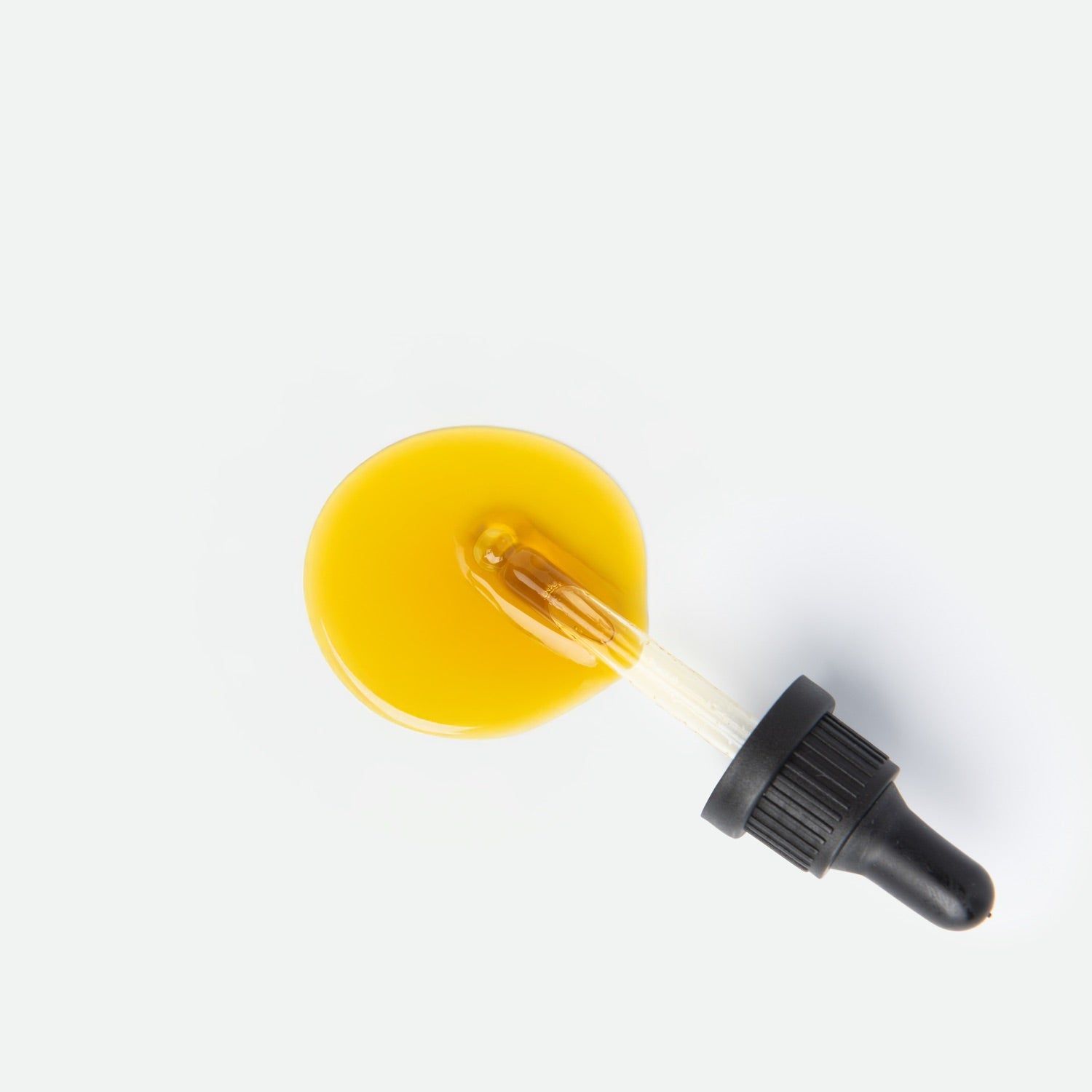 Goutte d'huile jaune avec pipette en verre et compte-gouttes noir sur fond blanc.