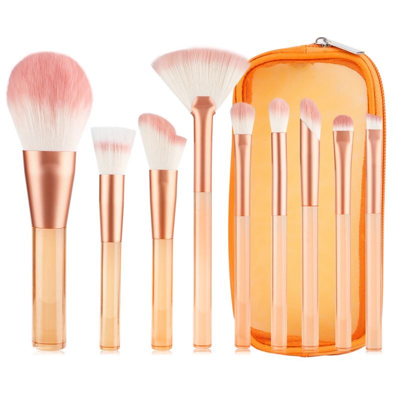 Ensemble de pinceaux de maquillage avec manches orange transparents, poils roses, dans une trousse orange.