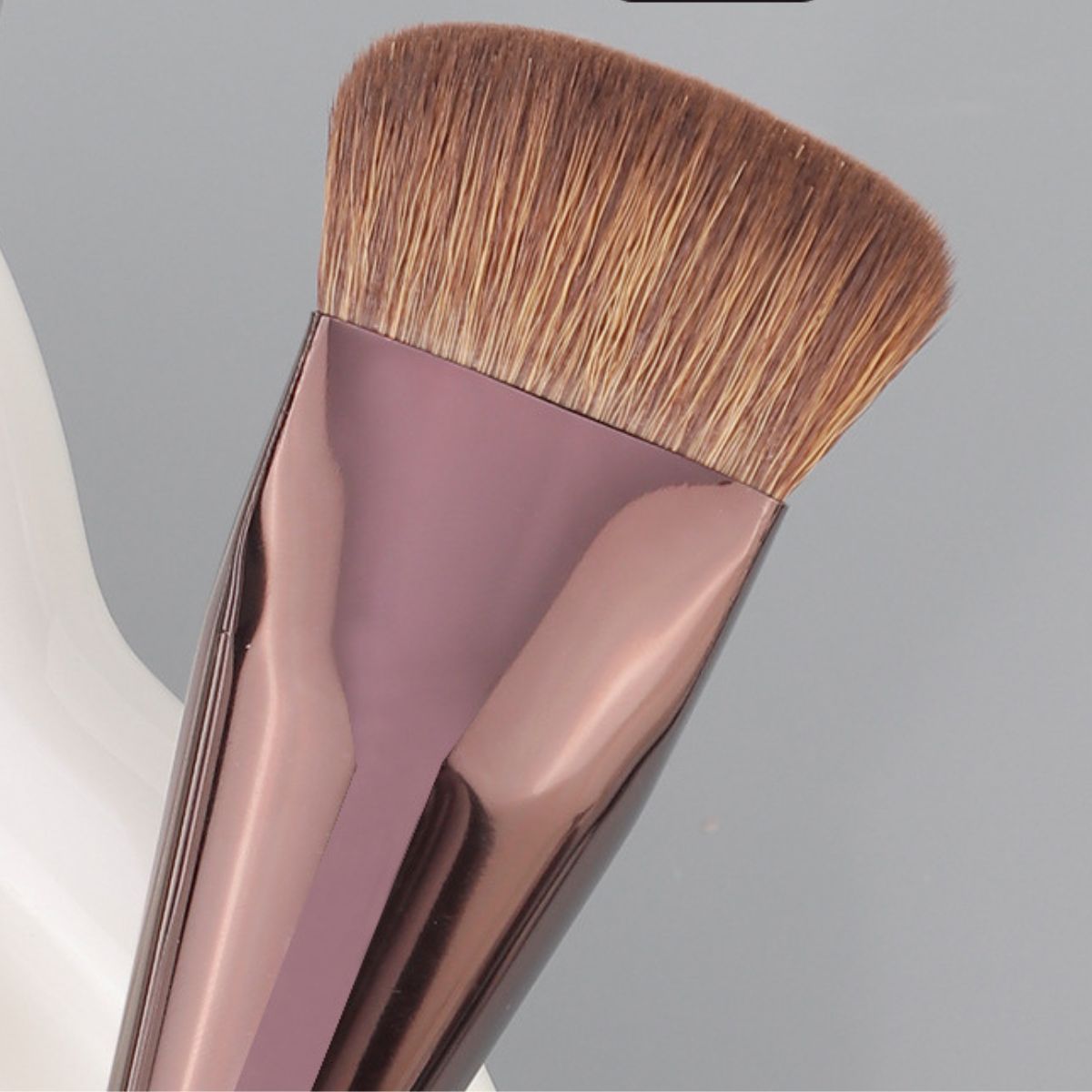 Pinceau de maquillage biseauté à dessus plat, manche couleur or rose, poils bruns denses.