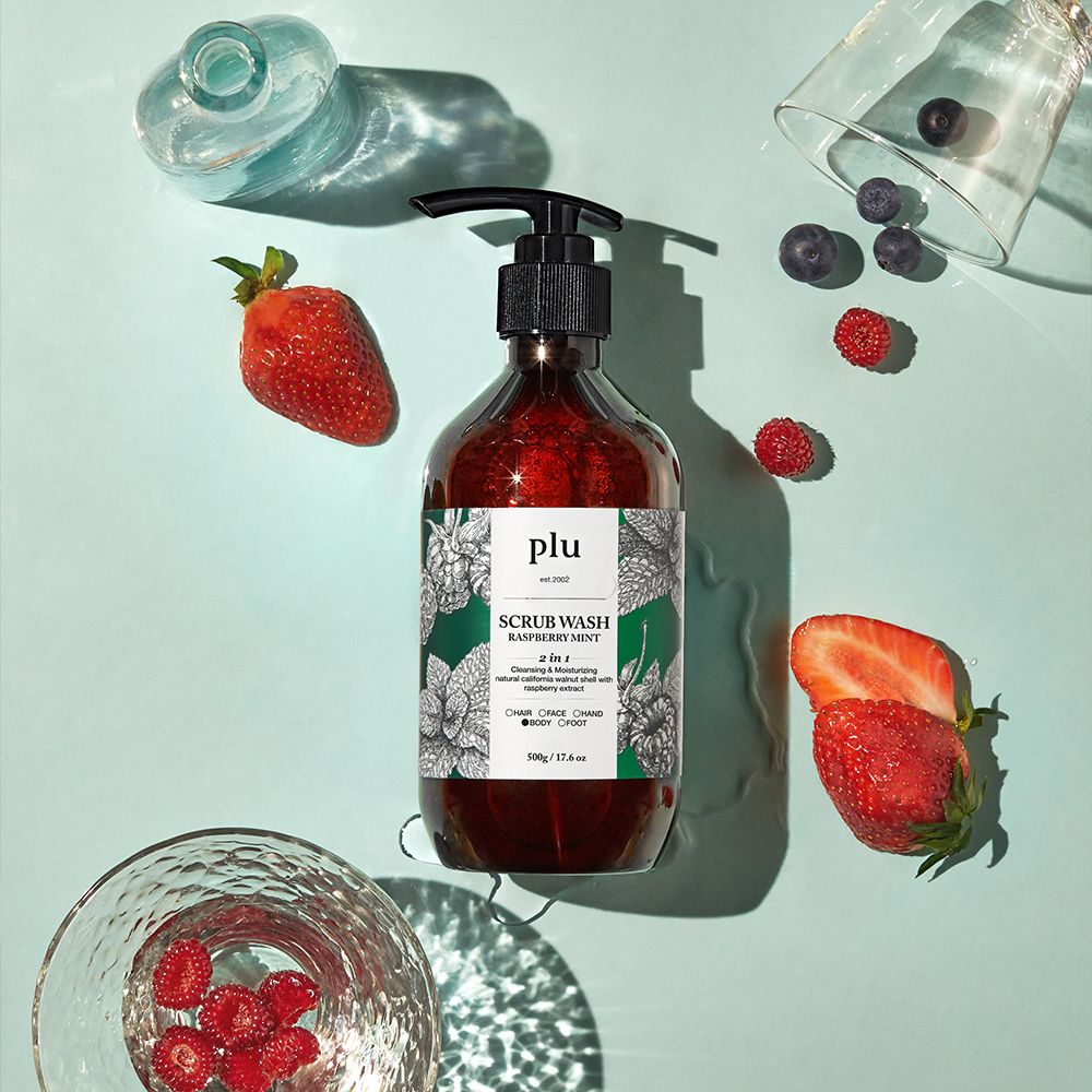 Flacon brun avec pompe noire. Inscription : PLU Scrub Wash Raspberry Mint. Fraises, framboises et myrtilles à côté.