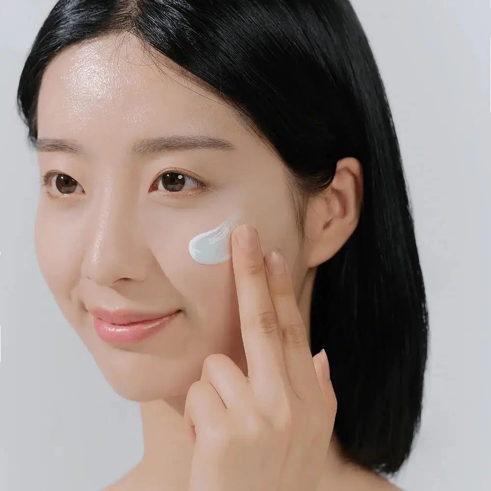 Femme appliquant de la crème sur le visage. Crème claire sur la peau. Peau claire. Cheveux noirs.