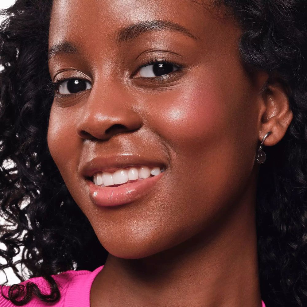 Femme avec blush rose sur les joues. Peau foncée, boucles noires.