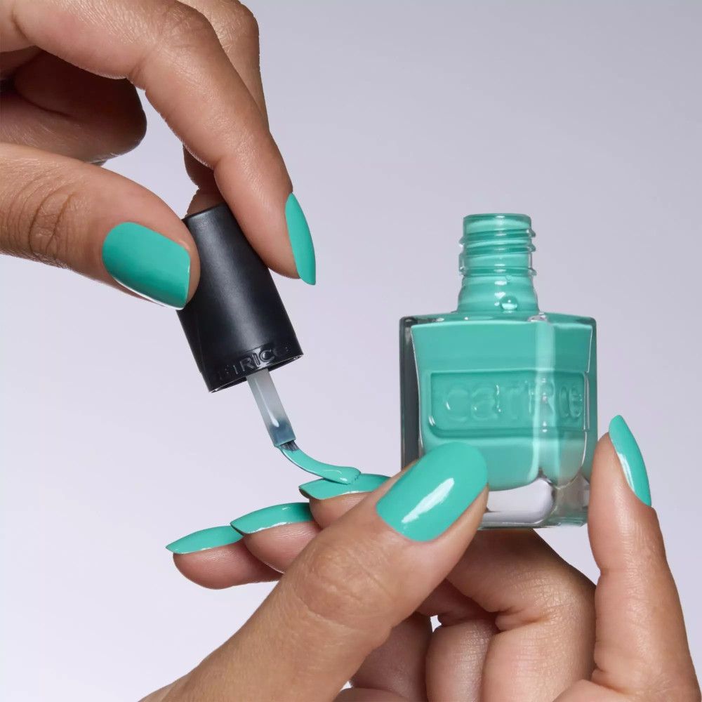 Mains tenant un flacon de vernis à ongles turquoise et un pinceau. Les ongles sont vernis avec le même vernis.