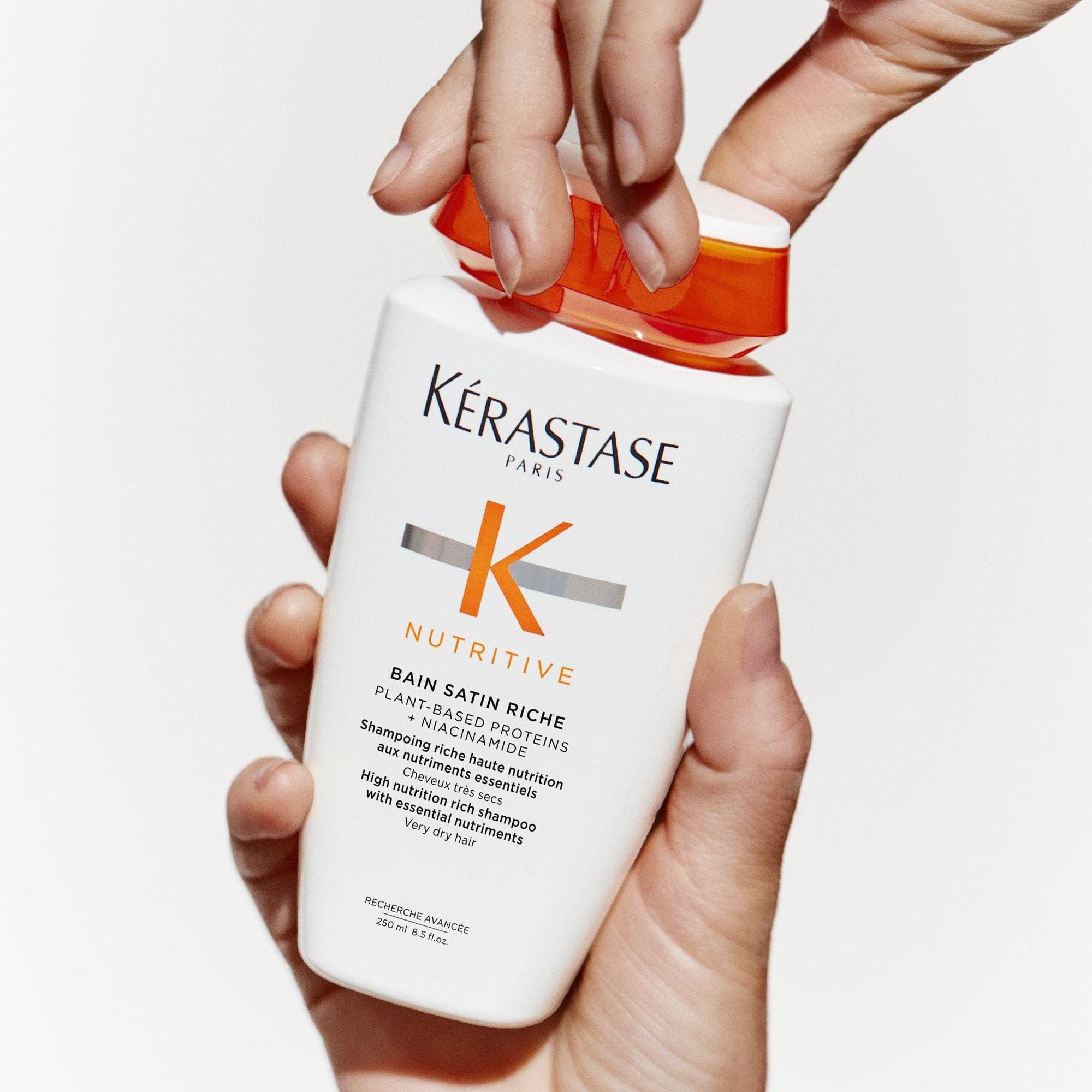 Handen die een Kérastase Nutritive Bain Satin Riche shampoofles openen.