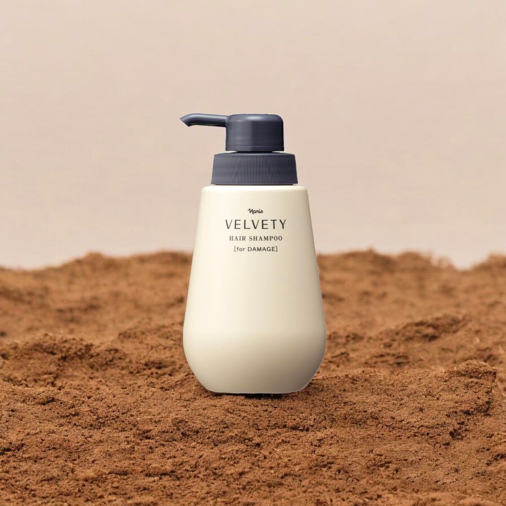 Beige VELVETY haarshampoofles met grijze pomp. Tekst: HAIR SHAMPOO [for DAMAGE]. Op bruine ondergrond.