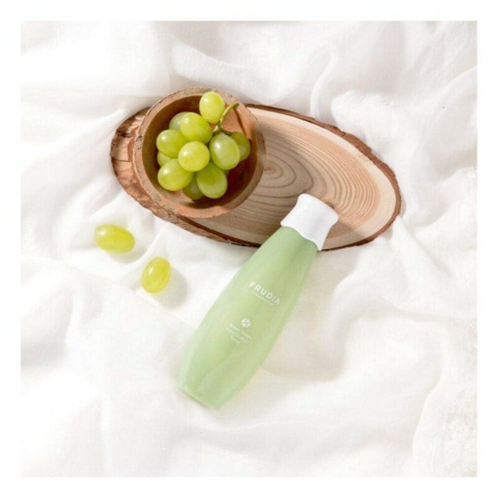 Groene fles met druivenextract en witte dop, naast een houten schaal met groene druiven.