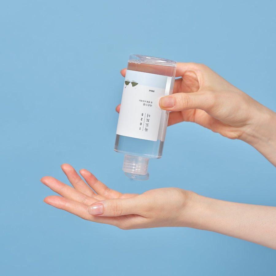 Flacon transparent avec étiquette blanche. Mains tenant le flacon au-dessus d'une paume. Fond bleu.