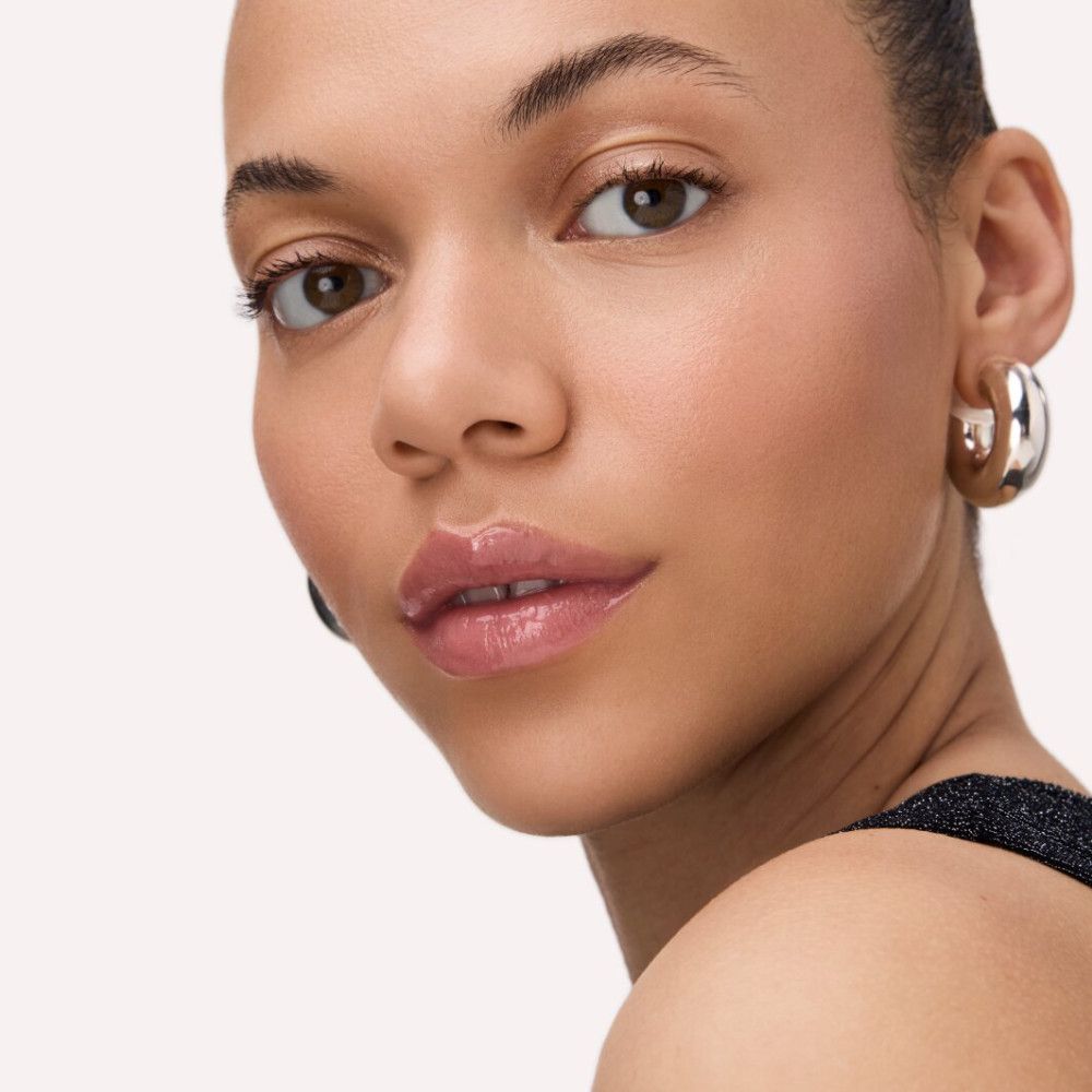 Portrait d'une femme avec du brillant à lèvres brillant sur les lèvres. Elle porte des boucles d'oreilles.