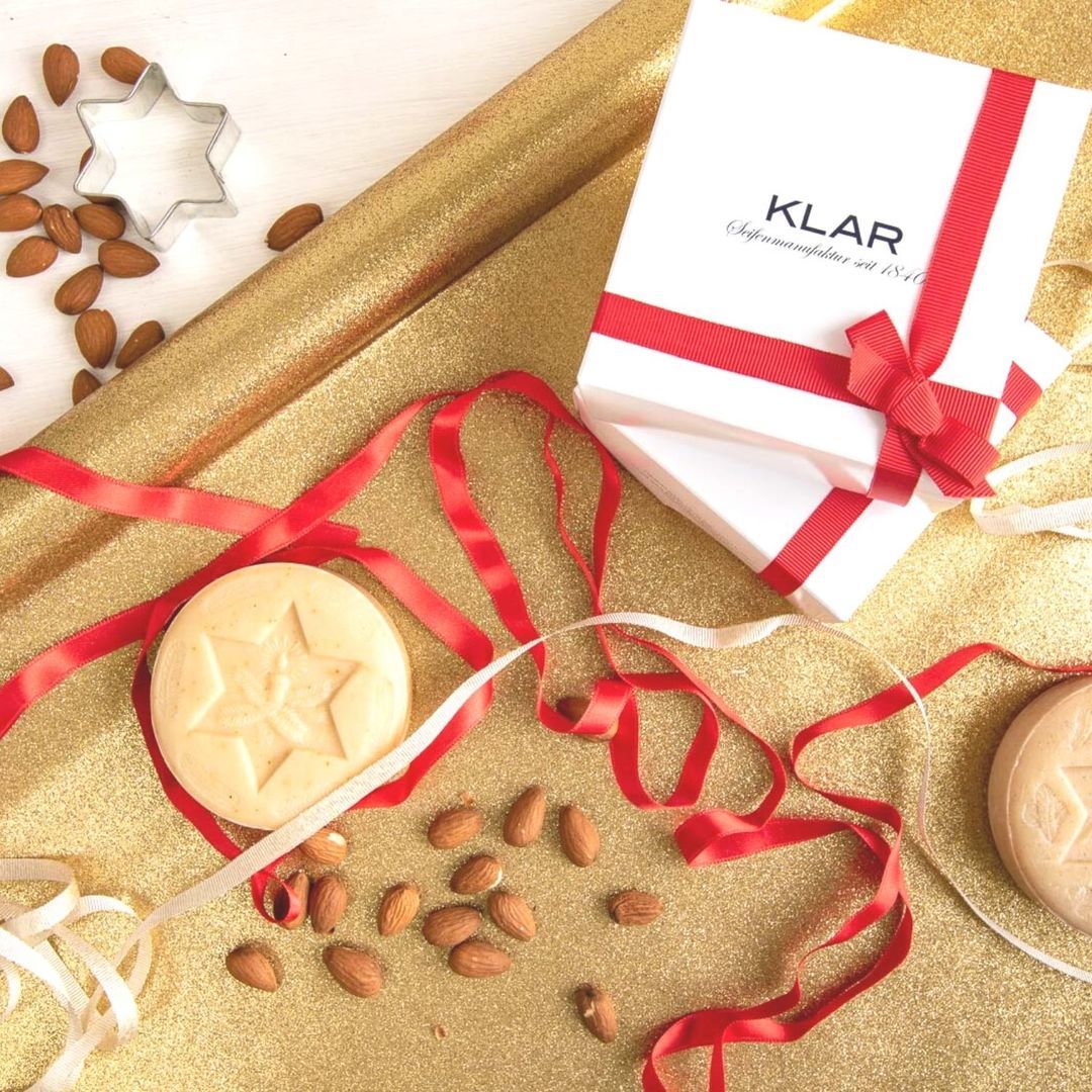 Savon rond avec motif étoile, amandes, emporte-pièce étoile et coffret cadeau avec ruban rouge. Fond doré.