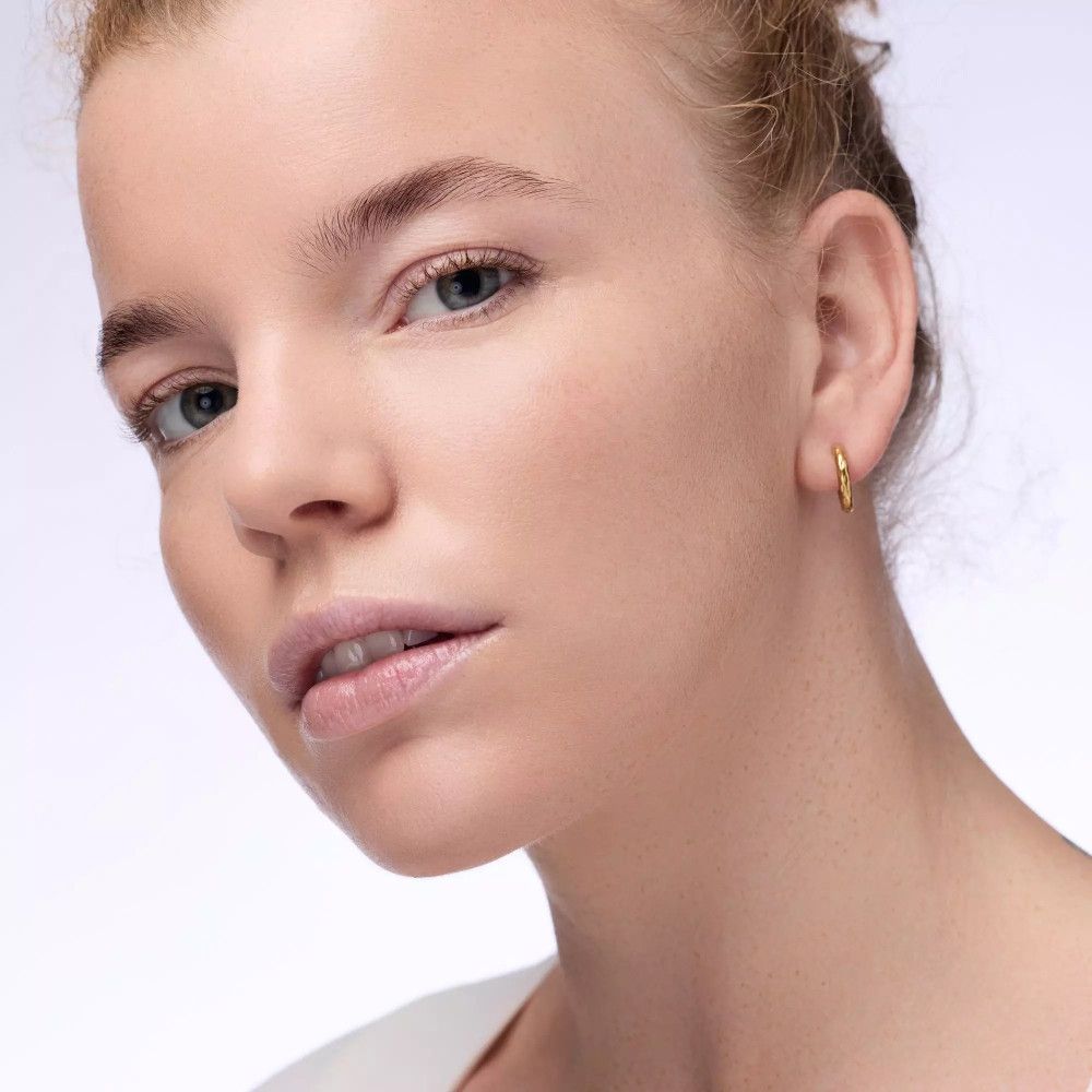 Portrait d'une femme avec boucles d'oreilles dorées. Peau uniforme.