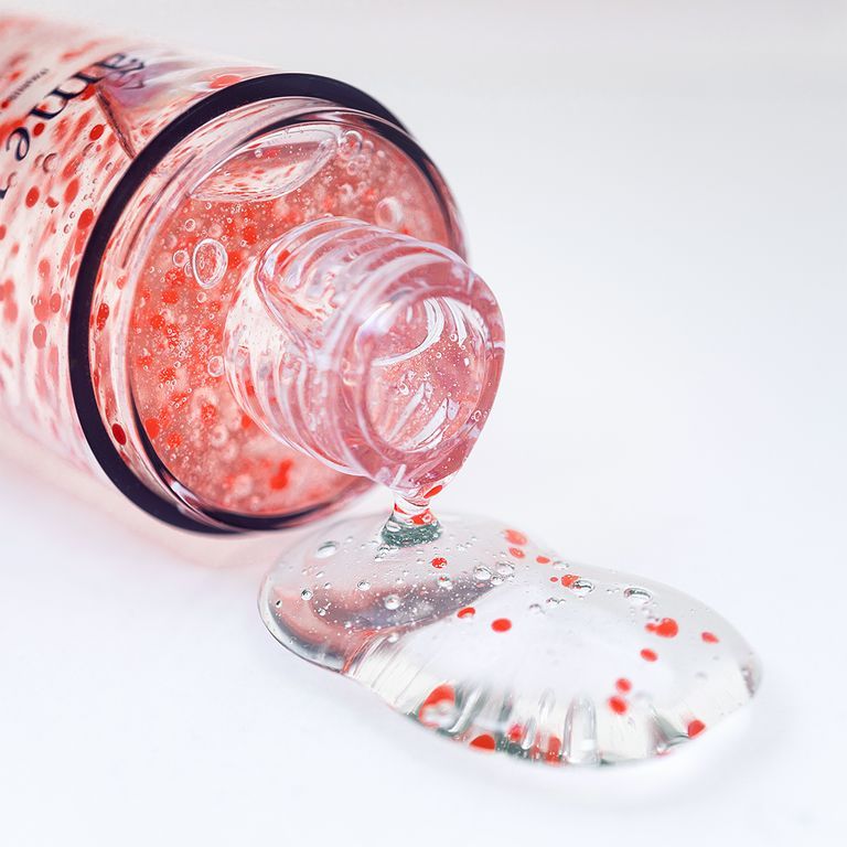 Un flacon de gel nettoyant avec particules rouges, du gel s'en échappe.