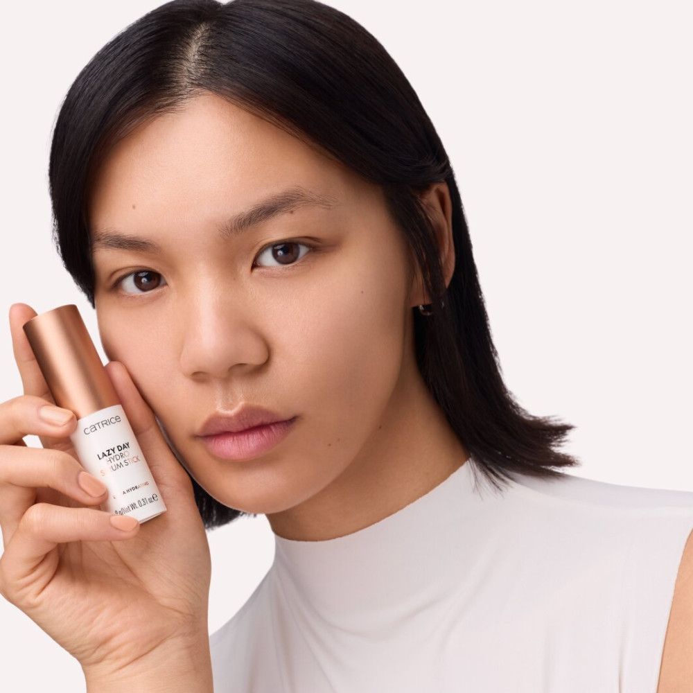 Femme tenant un stick de sérum. Inscription: Catrice, Lazy Day Hydro Serum Stick. Ultra Hydrating. 9g/Net Wt. 0.31 oz e. Bouchon or rose.