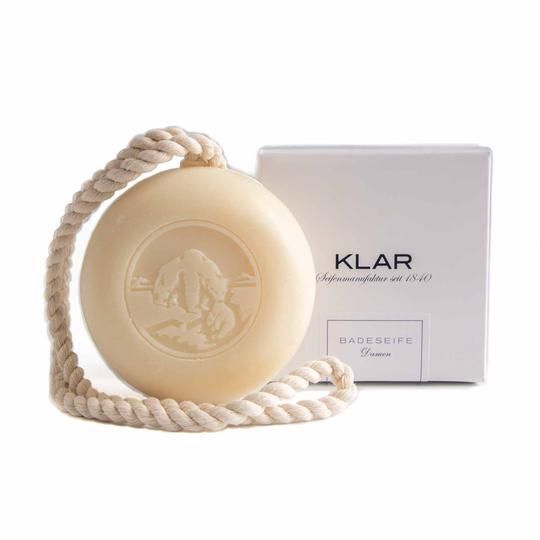 Savon rond avec cordon et gravure, à côté d'un emballage blanc avec l'inscription KLAR Badeseife Damen.