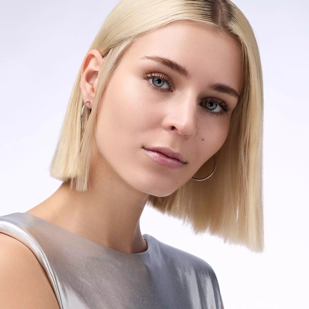 Portret van een vrouw met blond haar en blauwe ogen. Ze draagt oorbellen.