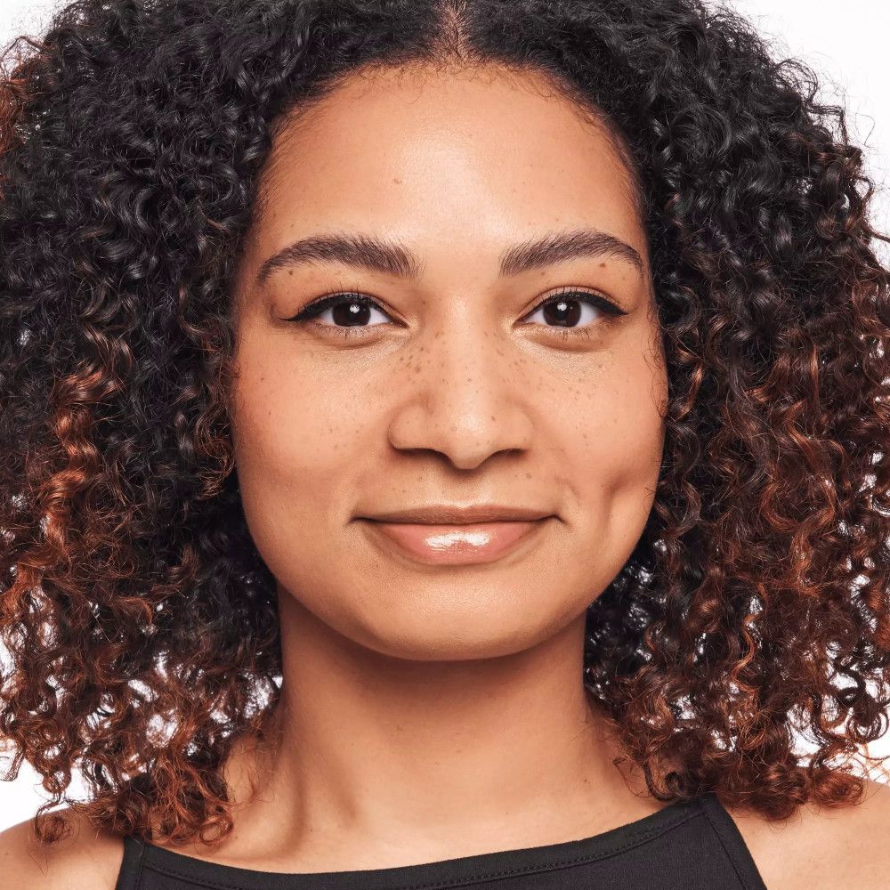 Close-up van een vrouw met krullen en lichte make-up. Ze heeft een glanzende lipstick en een subtiele eyeliner.