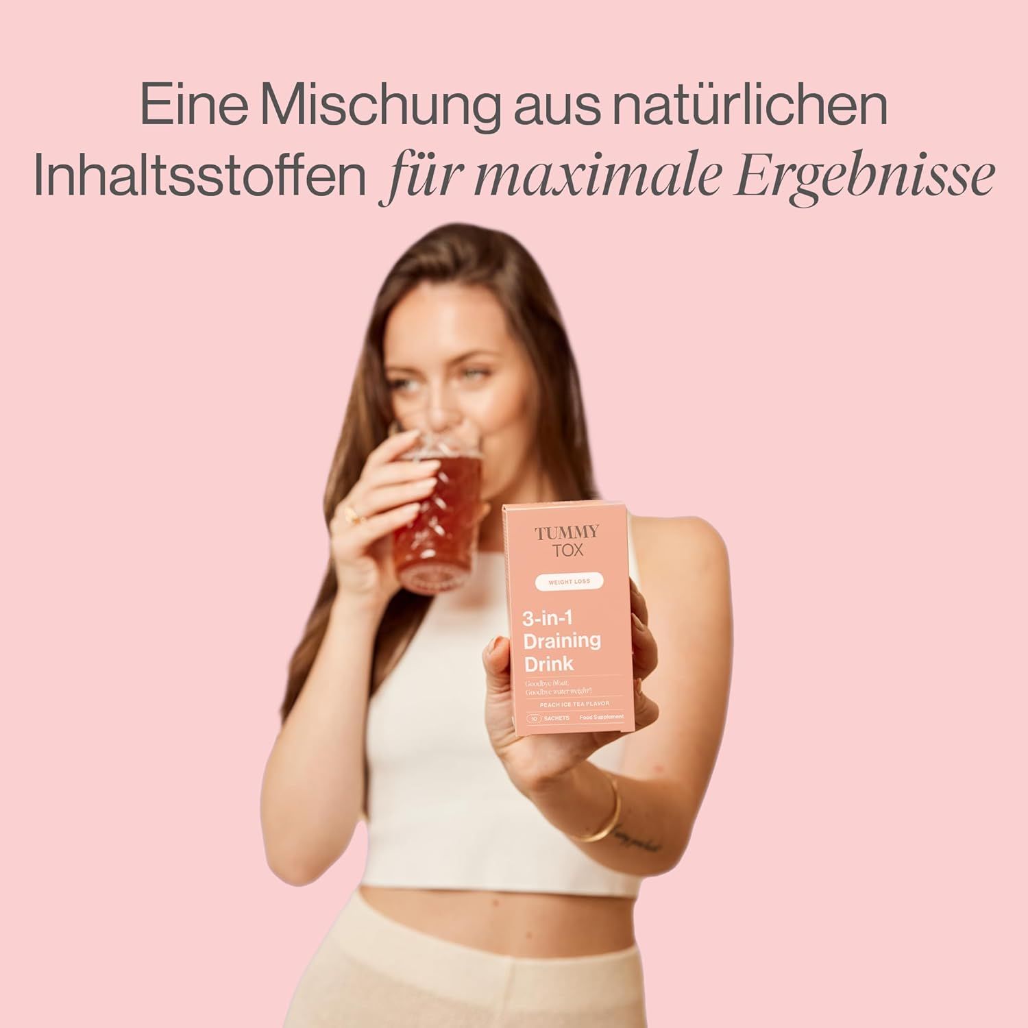 Femme buvant dans un verre. Elle tient un paquet avec l'inscription Tummy Tox 3-en-1 Draining Drink.