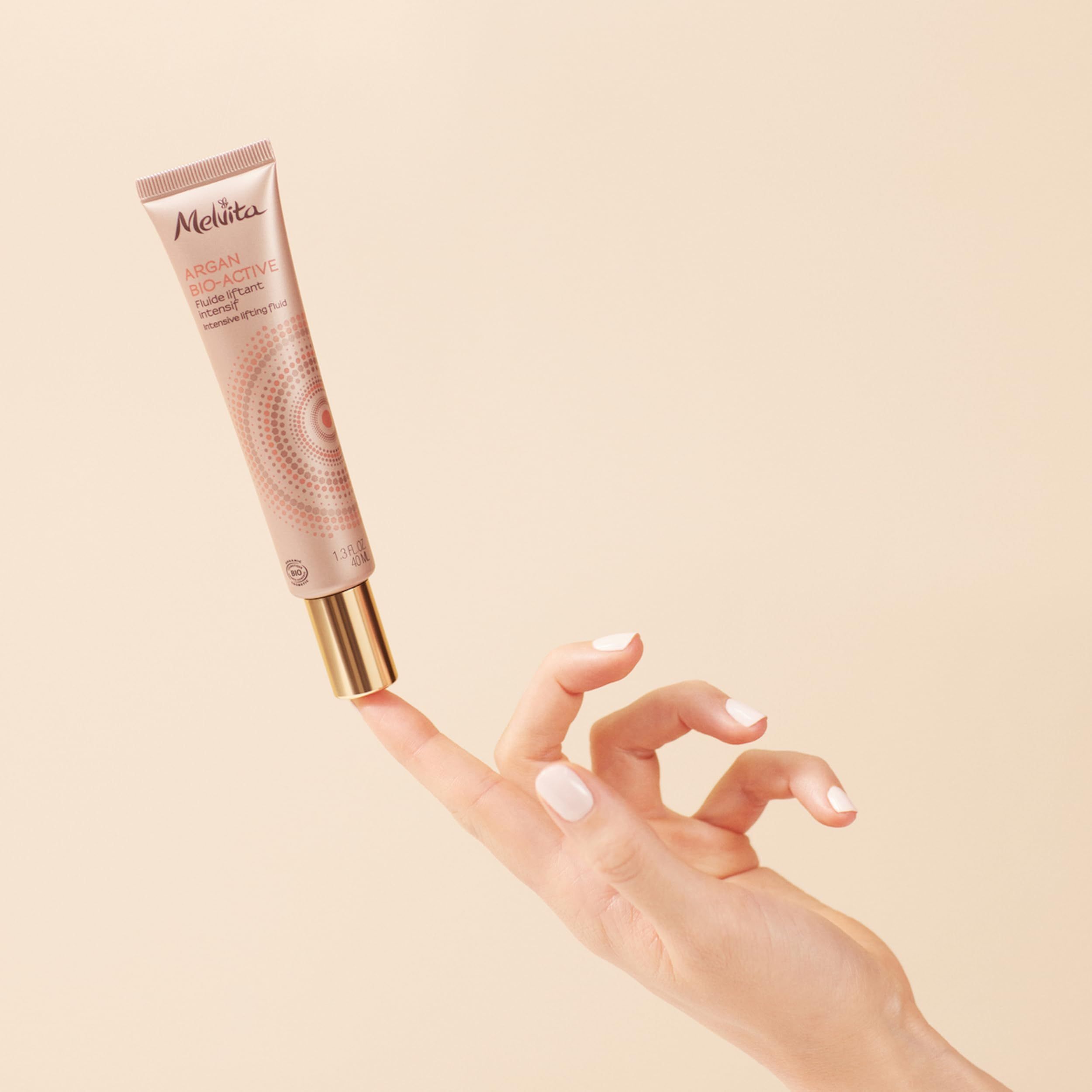 Tube beige et doré, tenu par une main. Inscription: Melvita, Argan Bio-Active, Fluide Liftant Intense Anti-âge.
