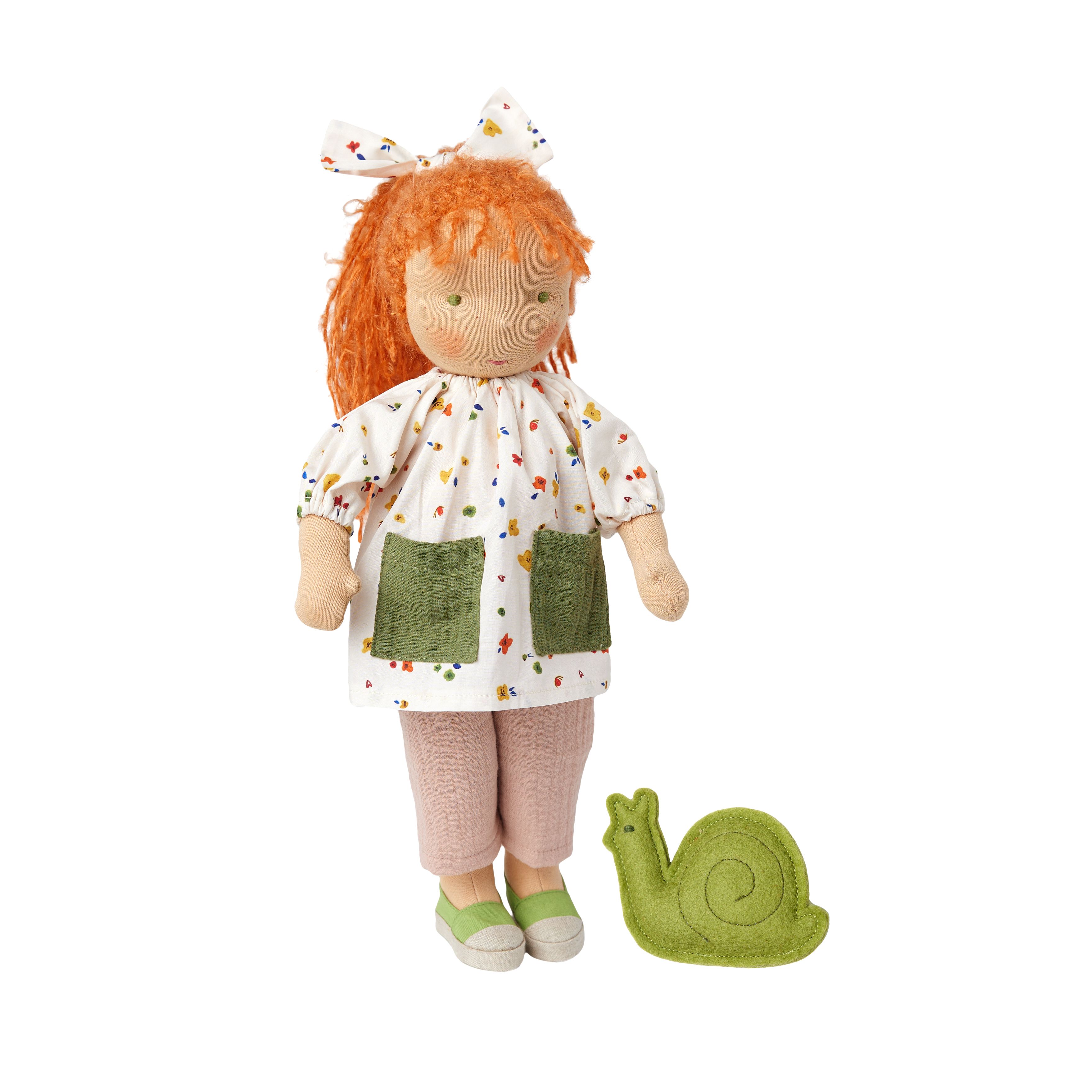 Stoffen pop met rood haar, witte jurk met bloemen, groene zakken en roze broek. Naast haar ligt een groene slak.
