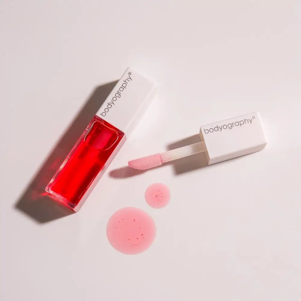 Lipglossflesje, applicator en roze productvlekken. Bodyography staat op de dop.
