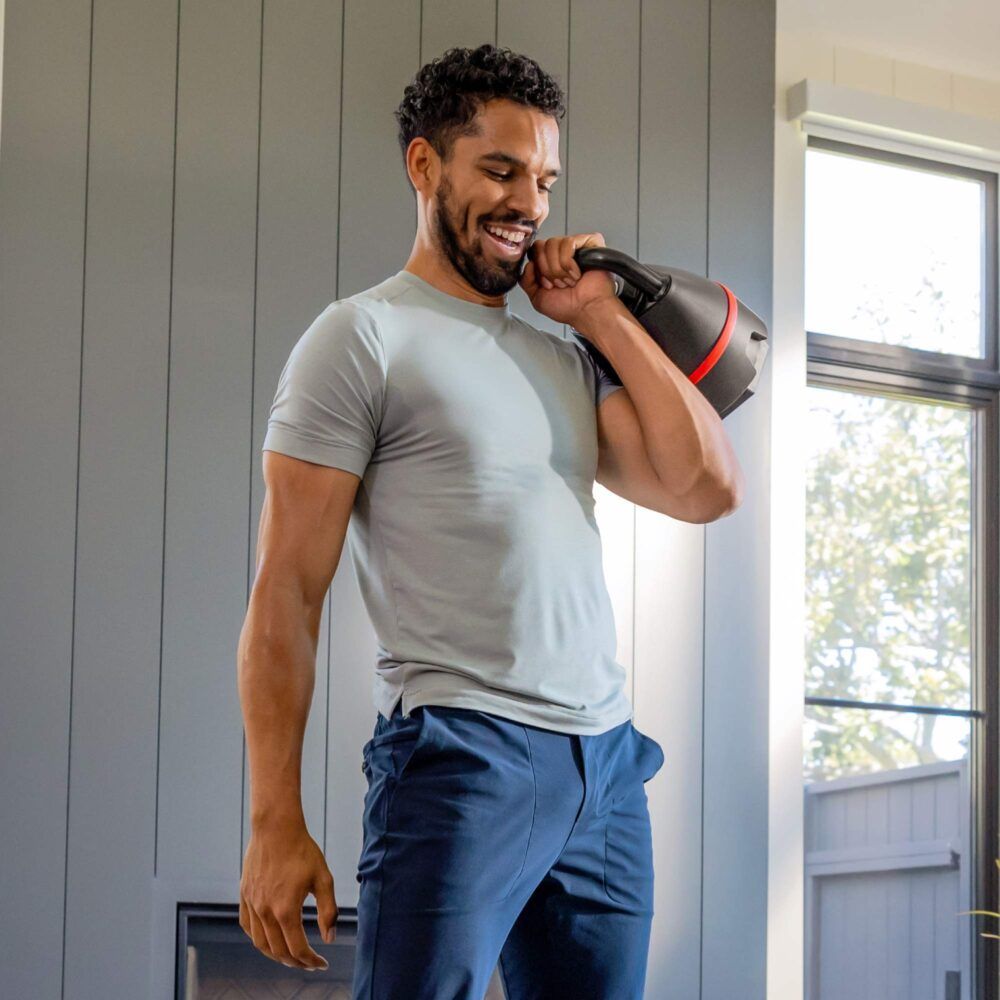 Man met kettlebell. Zwarte kettlebell met rode band. Bowflex-logo zichtbaar.