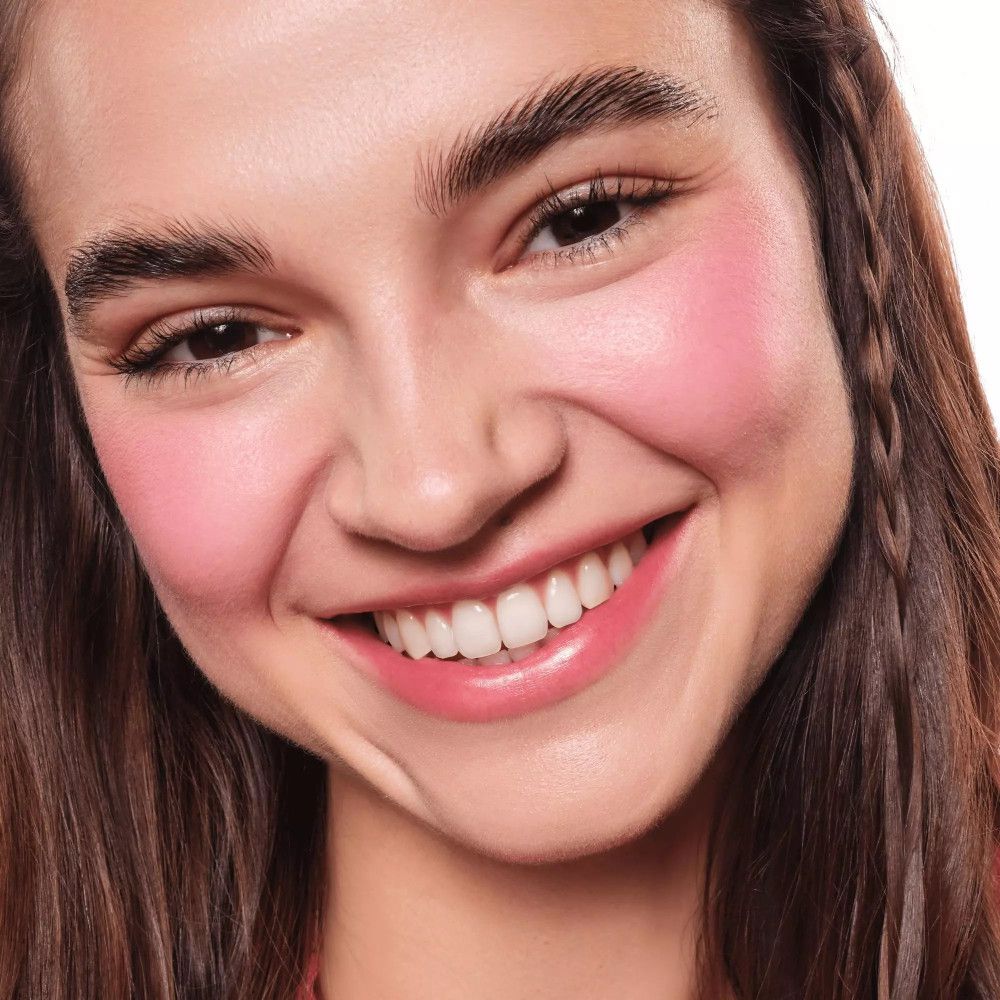 Femme avec blush rose sur les joues. Cheveux bruns, souriante.