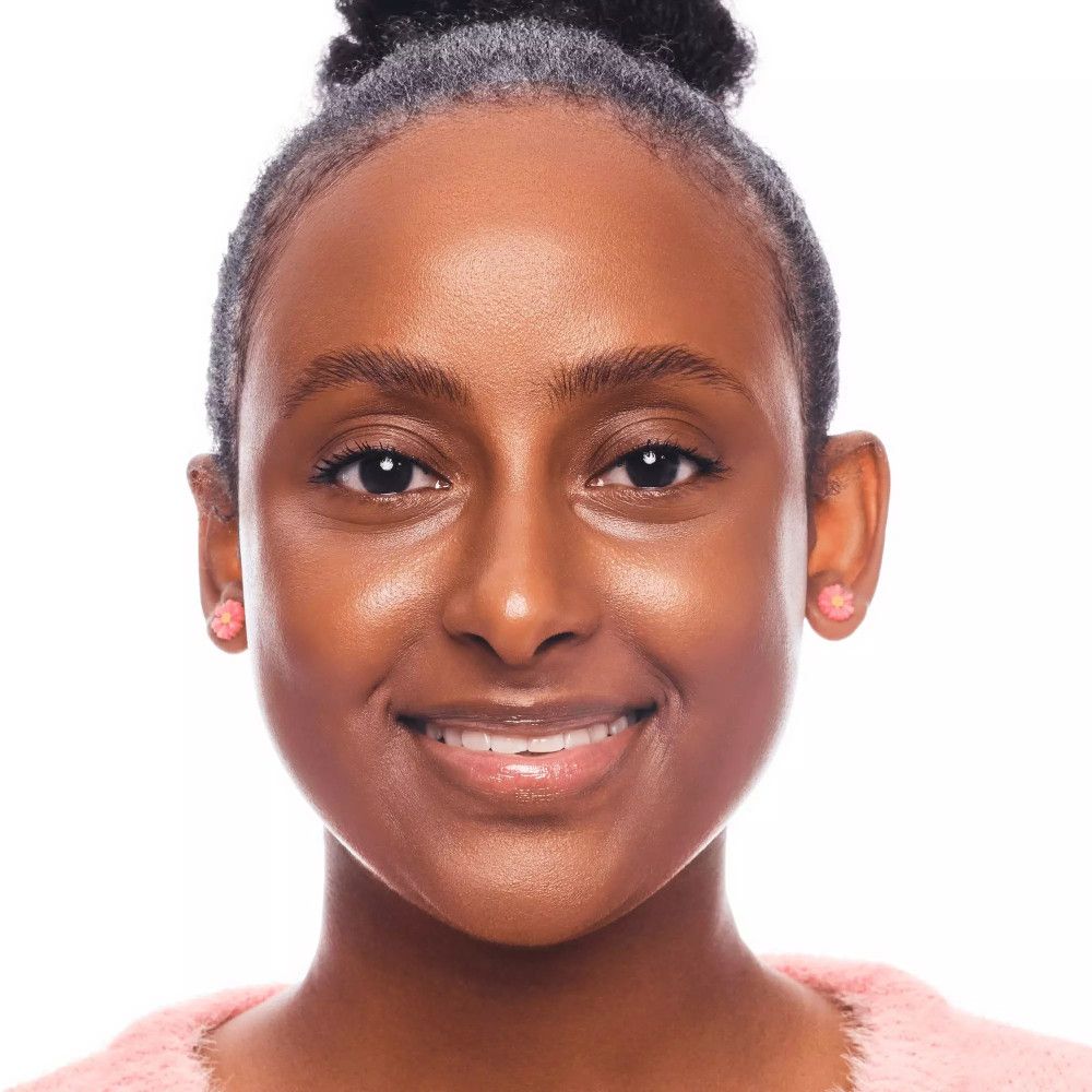 Portrait d'une femme à la peau bronzée. Elle porte des boucles d'oreilles roses et un pull rose. Ses cheveux sont attachés.