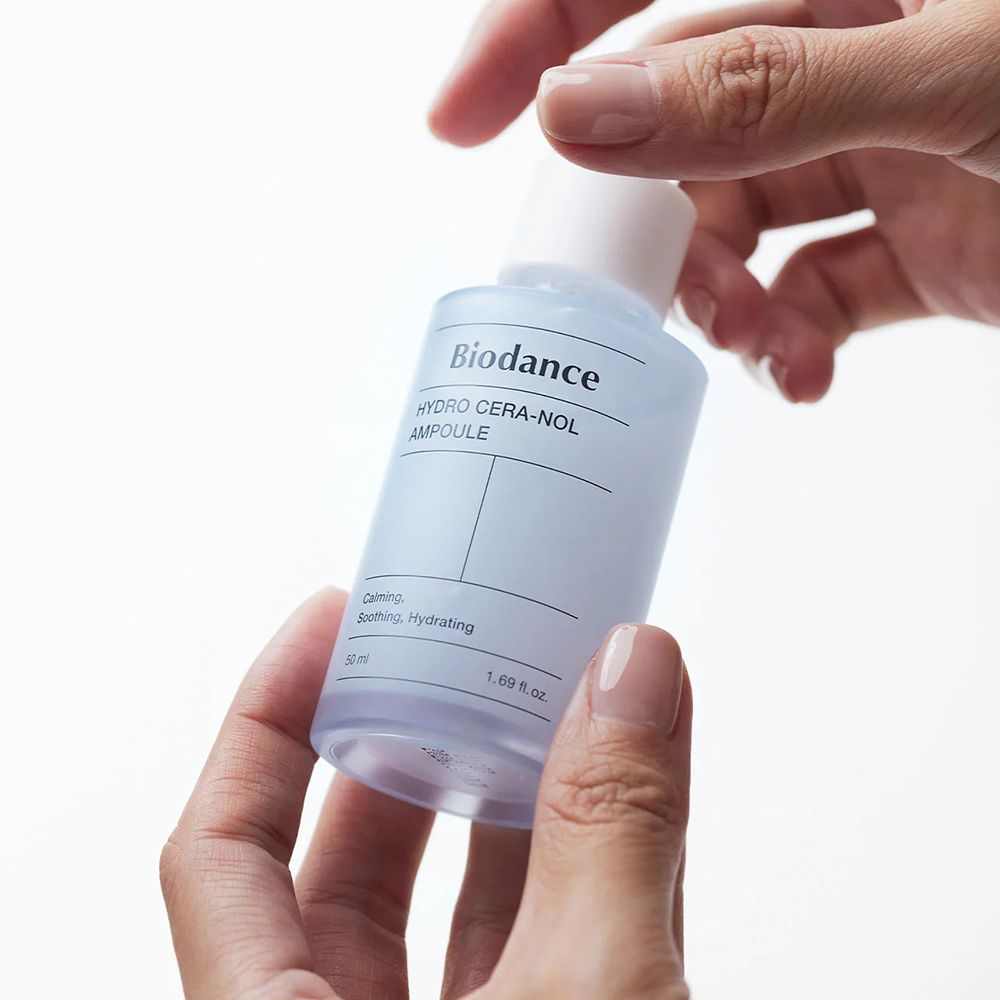 Handen houden een lichtblauw serumflesje met witte dop en pipet vast. Opschrift: Biodance Hydro Cera-nol Ampoule.