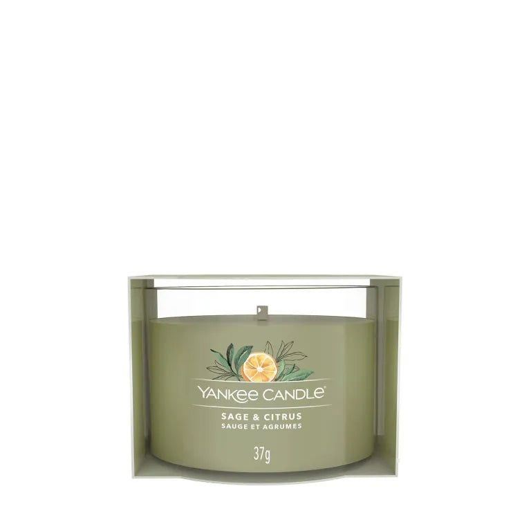Bougie verte dans un emballage. Inscription: Yankee Candle, Sage & Citrus, 37g. Décorée avec citron et herbes.