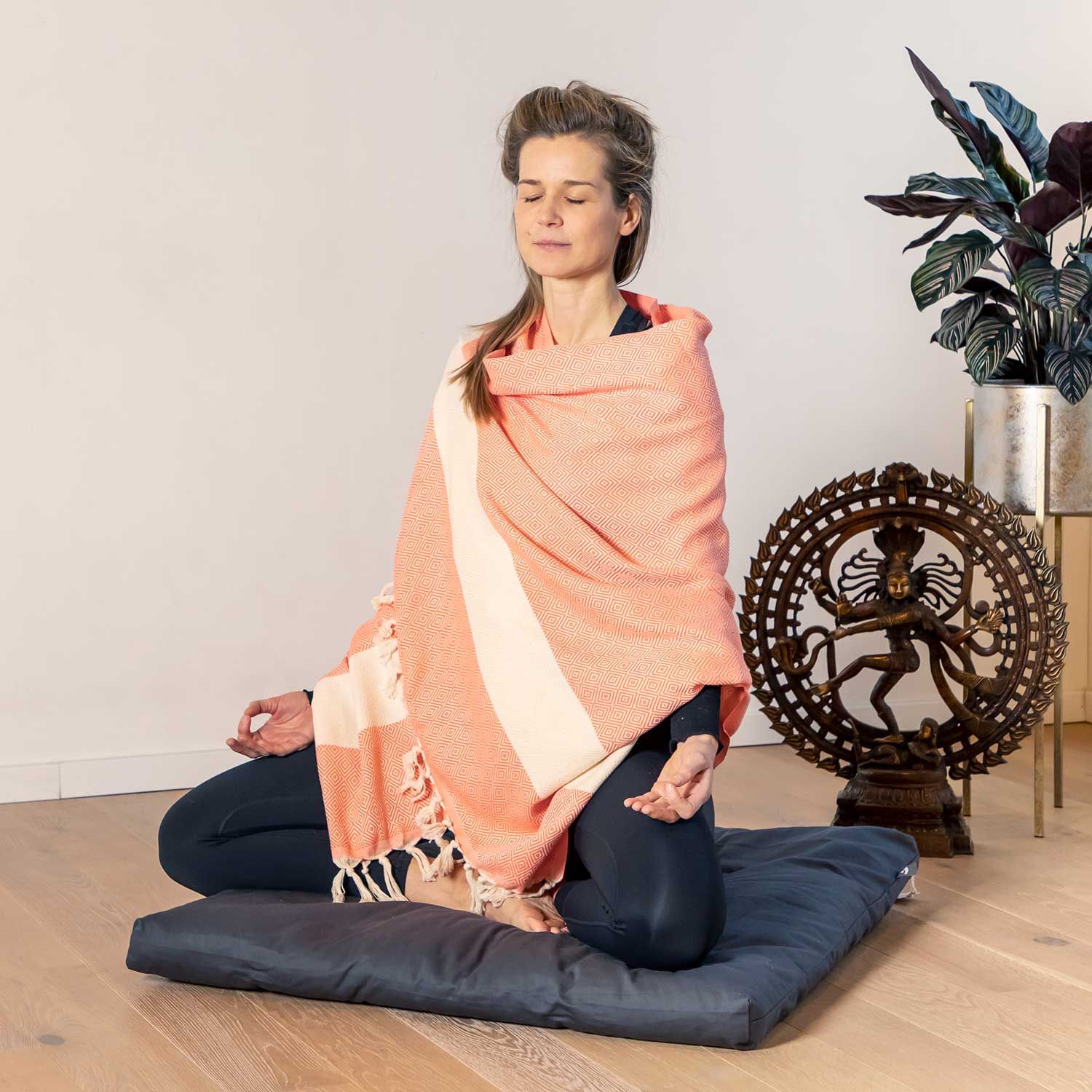 Vrouw zit in meditatiehouding, bedekt met hamamdoek, rood-oranje/natuur. Katoen.