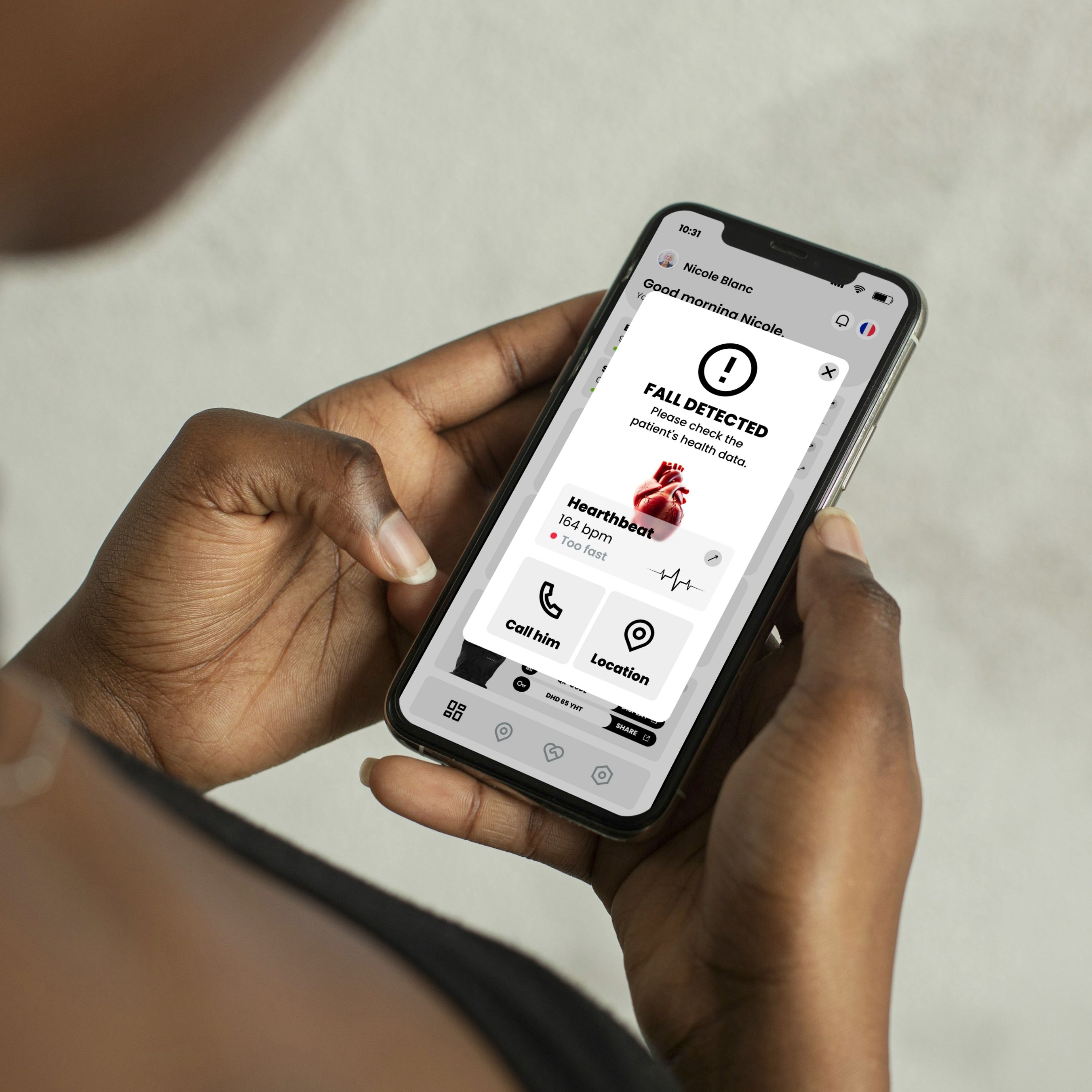 Personne tenant un smartphone avec une interface utilisateur. Message : "FALL DETECTED". Fréquence cardiaque : 164 bpm. Options : Appeler, Localisation.